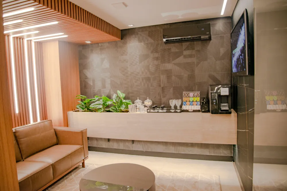 Sala de espera do consultório com sofá de couro, parede ripada iluminada e bancada de café